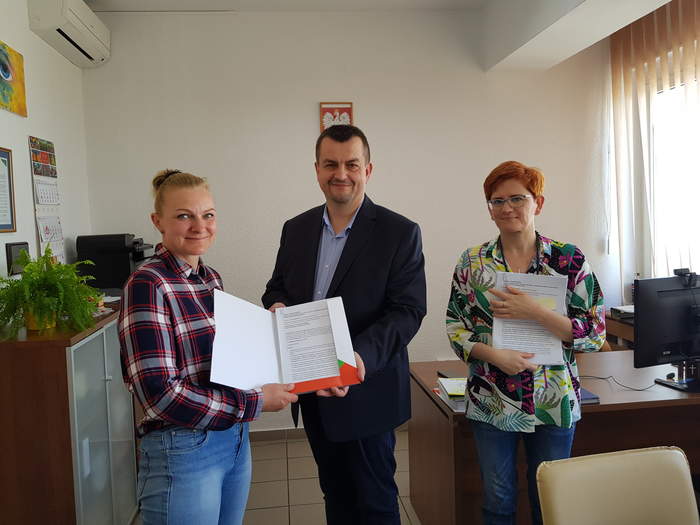 Pokaż zdjęcie: W Gabinecie Dyrektora stoją obok siebie osoby podpisujące umowę. Dyrektor trzyma umowę razem z Prezes Stowarzyszenia
