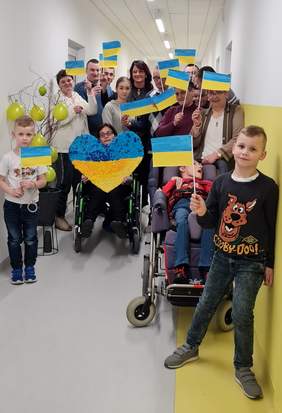 Pokaż zdjęcie: Podopieczni i przyjaciele Stowarzyszenia stoją na korytarzu trzymając w dłoniach flagi Ukrainy