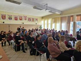 Pokaż zdjęcie: Zdjęcie uczestników konferencji siedzących na krzesełkach, ponad pięćdziesiąt osób.