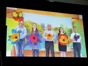 kard z filmu, grupa osób stoi na barwnym tle, trzymając kolorowe, duże kwiaty