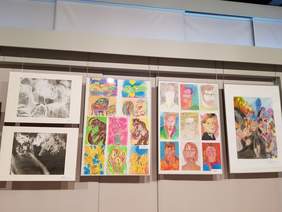 na ścianie wiszą prace, obrazy, przedstawiają głównie twarze, ale także konie, kwiaty, przeważają kolory