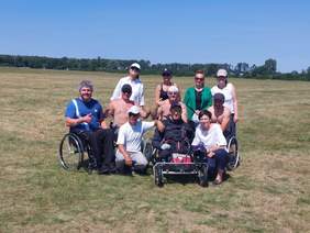Pokaż zdjęcie: Grupowe zdjęcie uczestników na wózkach inwalidzkich wraz z opiekunami i dyrektorem Oddziału Wielkopolskiego PFRON