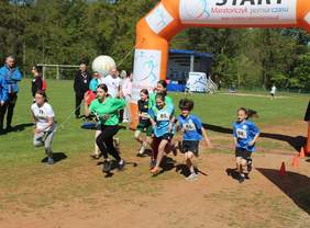 Pokaż zdjęcie: Grupa młodzieży w strojach sportowych na wytyczonym szlaku za startem rusza do biegu o złoty medal.