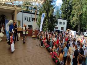 Pokaż zdjęcie: miejsce w plenerze wokół duża grupa osób ogląda co dzieje się na scenie, na której stoi grupa policjantów i dzieci 