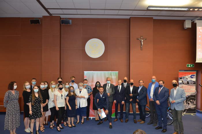 Pokaż zdjęcie: Liczna grupa osób w maseczkach, pozująca do zbiorowej fotografii. W tle baner konkursu i logo uniwersyteckie z łacińską nazwą: Universitas Cardinalis Stephani Wyszyński, Varsoviae. 