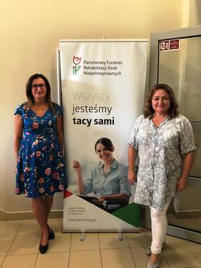 Pokaż zdjęcie: 2 osoby. Przedstawiciele Mazowieckiego i Podlaskiego Oddziału PFRON na tle banneru Funduszu pt. „Wszyscy jesteśmy tacy sami”. 