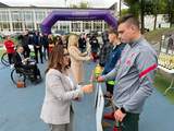 Wręczenie pucharu uczestnikowi zawodów sportowych na stadionie. W tle pozostali zawodnicy, organizatorzy oraz brama z napisem „Lubelskie. Z dumą wspieramy sport”.