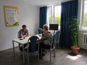 Mężczyzna siedzi za biurkiem i rozmawia z siedzącą naprzeciwko kobietą