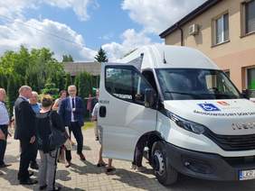 Pokaż zdjęcie: Przy białym aucie marki Iveco, które ma otwarte drzwi od strony pasażera stoją osoby, które oglądają nowe auto