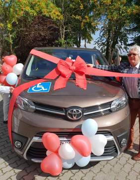 Pokaż zdjęcie: Mikrobus dla Osób Niepełnosprawnych marki Toyota obwiązany czerwoną kokardą.