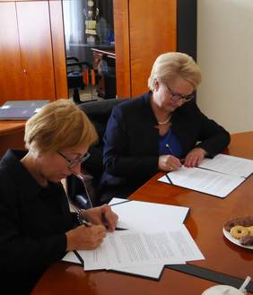 Pokaż zdjęcie: Dwie kobiety siedzące przy stoliku podpisują dokumenty