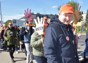 Pokaż zdjęcie: Ulicą idzie tłum ludzi. Niektórzy trzymają w dłonach transparenty z napisami: nadzieja, pomoc, akceptacja, integracja. W tle widać budynki i miejską zieleń.  