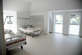 Pokaż zdjęcie: Zdjęcie dużej sali w szpitalu, w której stoją dwa szpitalne łóżka, wrażenie dużej przestrzeni