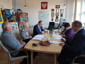 Przy jasnym stole w gabinecie dyrektora Oddziału PFRON z lewej strony siędzą dwaj mężczyźni i między nimi kobieta, z prawj strony mężczyzna i kobieta. Są w trakcie podpisywania dokumentów. Rozmawiają przy okazji.