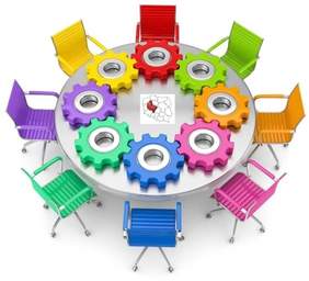 Pokaż zdjęcie: Osiem różnokolorowych krzeseł ustawionych wokół okrągłego stołu. Na stole ułożonych zostało osiem połączonych ze sobą trybów, odpowiadających kolorom krzeseł. Po środku stołu widnieje mapa Polski z wyodrębnionym województwem wielkopolskim, w kolorze czerwonym.