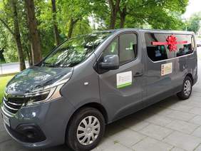 Pokaż zdjęcie: Nowy samochód dla uczestników Środowiskowego Domu Samopomocy w Bieczu z filią w Gorlicach przystosowany do przewozu osób z niepełnosprawnościami. Samochód z ozdobną kokardą oznaczony logotypem PFRON.