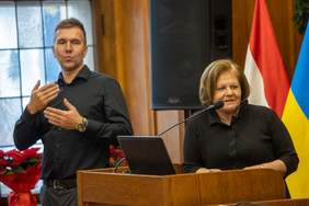 Przy mównicy przemawia Pani ALeksandra Gierej, a obok niej - po lewo - stoi i tłumaczy przemóienei tłumacz migowy