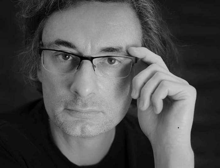 Pokaż zdjęcie: Mężczyzna w średnim wieku w okularach z długimi kręconymi włosami