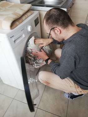 Pokaż zdjęcie: chłopak wkłada brudne rzeczy do pralki automatycznej uczy się samodzielnej obsługi 