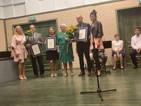 Pokaż zdjęcie: 6 osób, w tym 4 panie i 2 panów uroczyście ubranych stoi na scenie