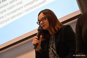 Pokaż zdjęcie: Prezes Stowarzyszenia "Po PROstu" w trakcie wystąpienia, na tle prezentacji, trzyma w ręku mikrofon