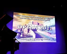 Wyświetlany na ekranie obraz: na tle widoku z Grudziądza napisy: na środku OPTAN 2022, na górze: XXIV Ogólnopolski Przegląd Twórczości Artystycznej Osób Niepełnosprawnych, na dole: Grudziądz, 4-7 sierpnia 2022 r.