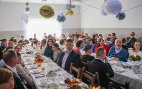 Pokaż zdjęcie: W sali WTZ przy uroczyście przystrojonych stołach zasiadają uczestnicy WTZ, którzy są ubrani odświętnie