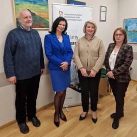 Pokaż zdjęcie: Trzy kobiety i jeden mężczyzna pozują do zdjęcia. W tle obrazy wiszące na ścianie w sali konferencyjnej.