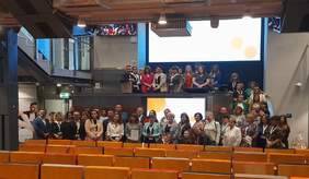 Pokaż zdjęcie: duża sala kinowa na której stoją goście i nagrodzeni laureaci pozują do zdjęcia 