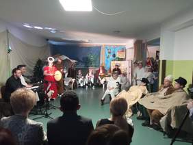 Pokaż zdjęcie: Zdjęcie robione z widowni w kierunku przedstawienia. Na scenie śpiewane są kolędy. Dzieci przebrane za aniołki, pasterzy i zwierzą stoją wokoło Dzieciątka Jezus.