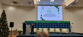 Pokaż zdjęcie: Na scenie przy mównicy stoi Pan Krzysztof Czechowski Koordynator ds. dostępności ZUS oraz Pani Anna Wandzel Dyrektor Oddziału Mazowieckiego PFRON, w tle slajd prezentacji konferencji na temat wdrażania i monitorowania dostępności w instytucjach publicznych dla osób ze szczególnymi potrzebami. W lewym górnym rogu logo ZUS, na dole slajdu logo partnerów.