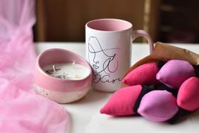 Pokaż zdjęcie: Przedmioty wykonane przez podopiecznych ZAZ - na stole ułożone obok siebie leżą świeczka, zdobiony kubek oraz ręcznie wykonane tulipany 