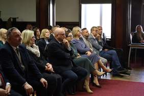 Pokaż zdjęcie: Osoby zaproszone na wydarzenie siedzące na krzesełkach.