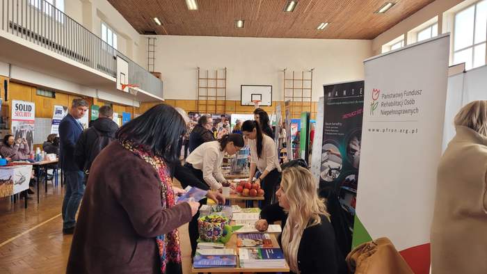 Pokaż zdjęcie: Przy stoisku stoją osoby zainteresowane ofertą funduszu.