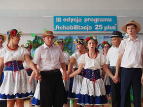 Występ, kobiety i mężczyźni w strojach ludowych, trzymają się za ręce, śpiewają