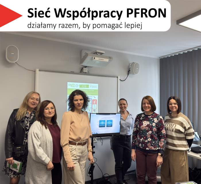 Pokaż zdjęcie: Na górze, na białym tle, widoczny jest czerwony, trójkątny element. Obok znajduje się tekst: 'Sieć Współpracy PFRON', a poniżej napis: 'działamy razem, by pomagać lepiej'. Zdjęcie grupowe sześciu kobiet stojących w sali szkoleniowej przy tablicy. Pomieszczenie ma jasnoszare ściany, na ścianie widać projektor oraz dwa głośniki. Po prawej stronie są pionowe żaluzje przy oknie i fragment biurka. Kobiety stoją w jednym rzędzie, uśmiechnięte. Na tablicy za nimi jest wyświetlony slajd