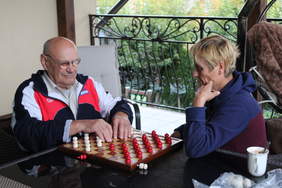 Pokaż zdjęcie: Kobieta i mężczyzna rozgrywają partię szachów dla niewidomych i słabowidzących. Pan trzyma dłonie na szachownicy, na której są białe i czerwone figury. 