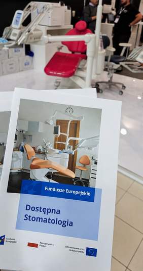 Pokaż zdjęcie: Ulotka projektu „Dostępna stomatologia” realizowanego w ramach Funduszy Europejskich. Na okładce zdjęcie wyposażonego gabinetu stomatologicznego oraz logotypy programu. W tle, na stoisku targowym, prezentowany jest nowoczesny fotel dentystyczny i sprzęt stomatologiczny.