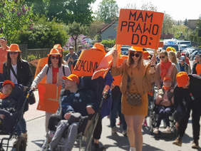 grupa uczestników, z przodu dwie osoby na wózkach inwalidzkich, kobieta ubrana na pomarańczowa trzyma pomarańczową kartkę z napisem mam prawo do: