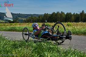 Pokaż zdjęcie: kobieta na trzykołowym leżącym rowerze, rękoma wprawia w ruch koła