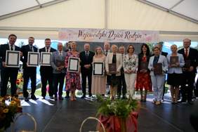 Pokaż zdjęcie: Na scenie w rzędzie stoi duża grupa osób, trzymają przed sobą dyplomy, pozują do pamiątkowego zdjęcia