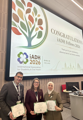 Pokaż zdjęcie: Trzy osoby prezentują certyfikaty iADH Fellowship 2026 na scenie konferencji iADH w Dublinie, na środku stoi prof. dr hab. Karolina Gerreth - brunetka na tle ekranu z gratulacjami dla wyróżnionych Fellows.