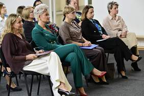 Pokaż zdjęcie: Trzy kobiety siedzą na widowni podczas Konferencja „Technologie asystujące wspierające wczesne wspomaganie rozwoju dziecka”. W tle widać licznie zgromadzonych uczestników wydarzenia.