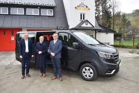 Pokaż zdjęcie: Elegancko ubrani: kobieta i dwóch mężczyzn stoją na tle nowego samochodu przystosowanego do przewozu osób niepełnosprawnych.