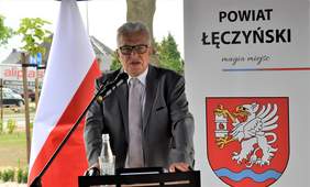 Pokaż zdjęcie: Na tle polskiej flagi i godła powiatu łęczyńskiego przemawia przy mównicy prezes zarządu PFRON Krzysztof Michałkiewicz
