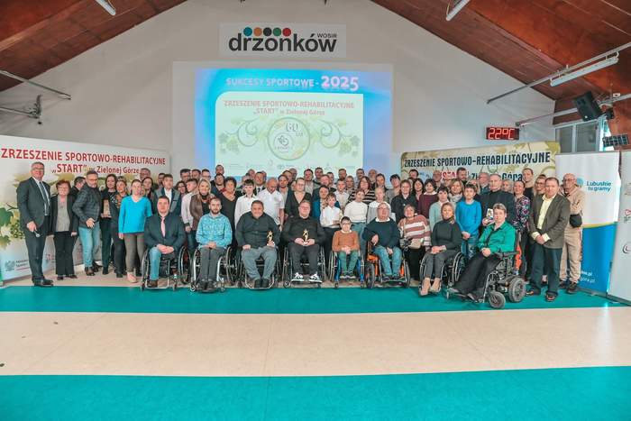 Pokaż zdjęcie: W hali Wojewódzkiego Ośrodka Sportu i Rekreacji w Zielonej Górze-Drzonkowie uczestnicy spotkania stoją do okolicznościowego zdjęcia na tle prezentacji "Start" Zielona Góra