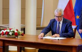 Pokaż zdjęcie: Mężczyzna podpisuje dokument, w tle flagi Polski i Unii Europejskiej