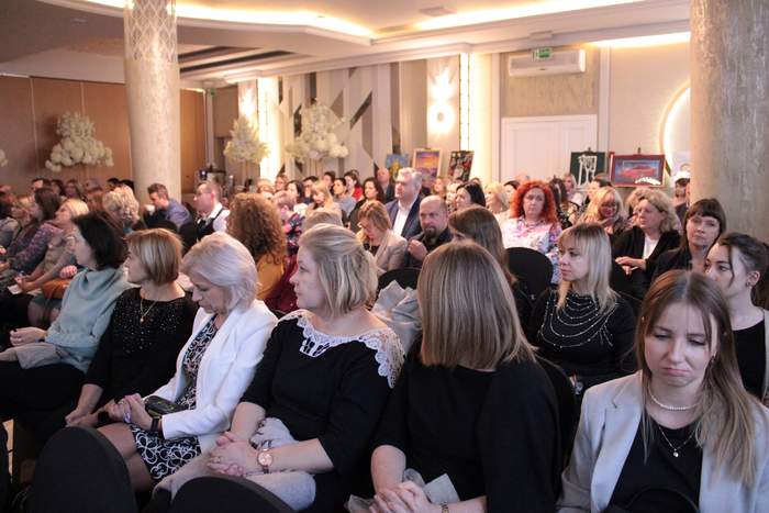 Pokaż zdjęcie: Zdjęcie sali konferencyjnej, układ sali kinowy, na krzesłach siedza uczestnicy konferencji, w tle widać sztalugi na których umieszczone są prace plastyczne osób z niepełnosprawnościami