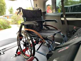 Pokaż zdjęcie: W busie na tyle samochodu stoi zapięty ciemny wózek inwalidzki.