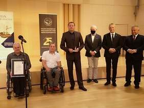 6 mężczyzn na scenie dwóch na wózkach inwalidzkich, 4 stoi, na scenie